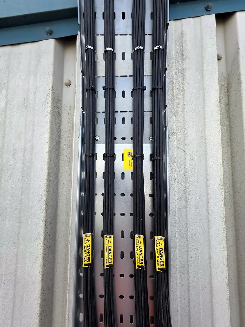 Vertical tray carrying labelled DC cables down the wall